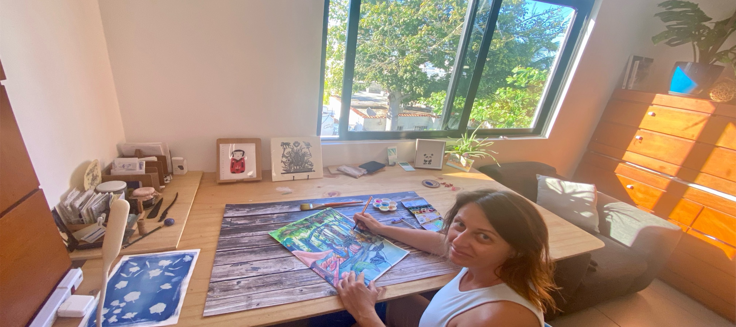 Amandine painting at a studio table in warm natural light.