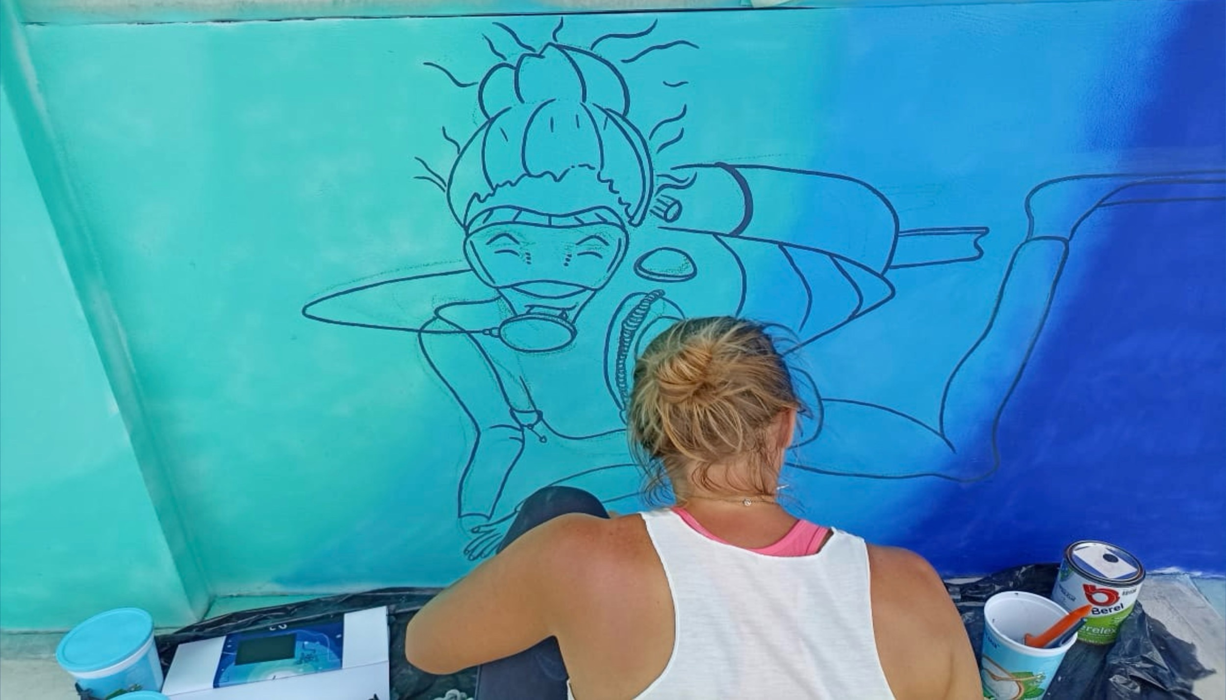 Amandine painting a blue mural sketch on a wall.