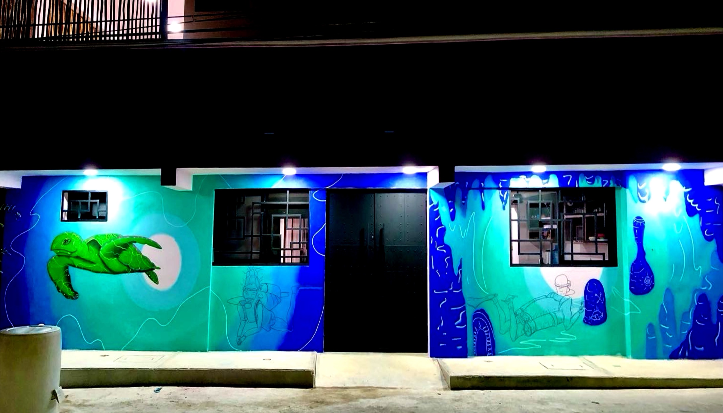 Large blue and green exterior mural lit at night.